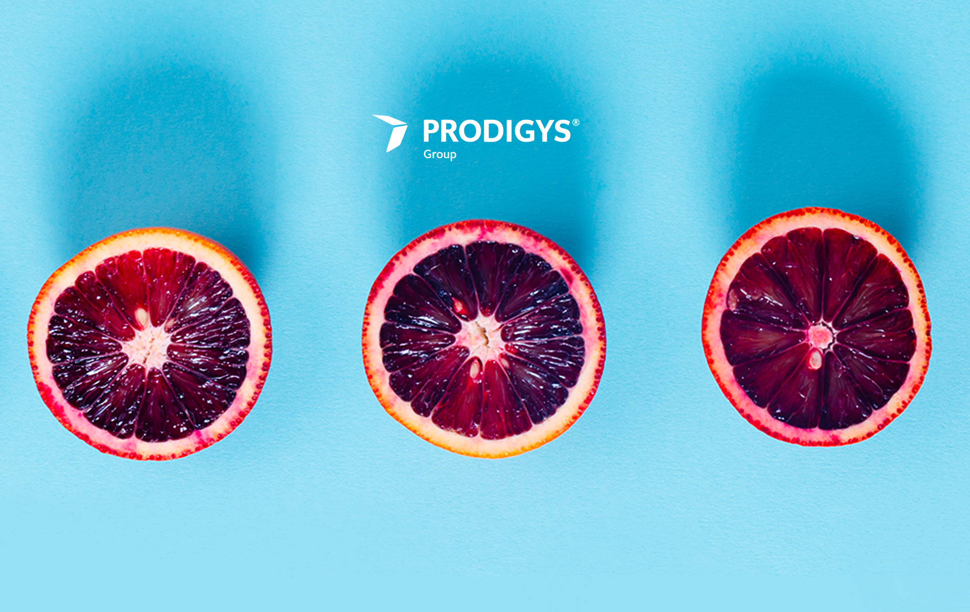 Tre mezze arance rosse disposte in fila su sfondo azzurro, viste dall’alto. In alto al centro compare il logo ‘Prodigys Group’.