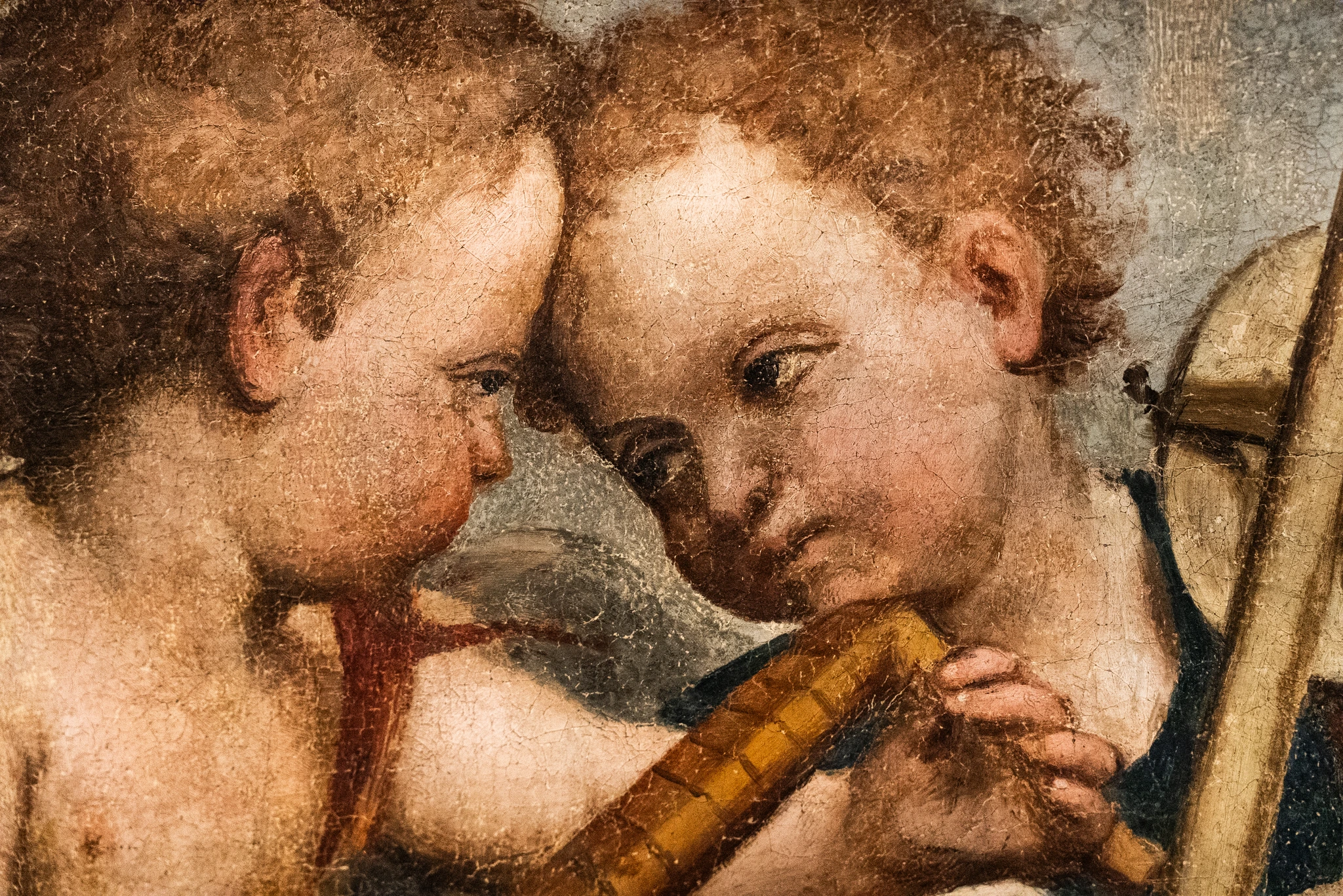 Dettaglio ravvicinato di un dipinto che raffigura due figure infantili con capelli ricci, avvicinate testa contro testa. Una delle figure tiene tra le mani un piccolo strumento musicale a fiato. La superficie pittorica presenta una trama visibile.