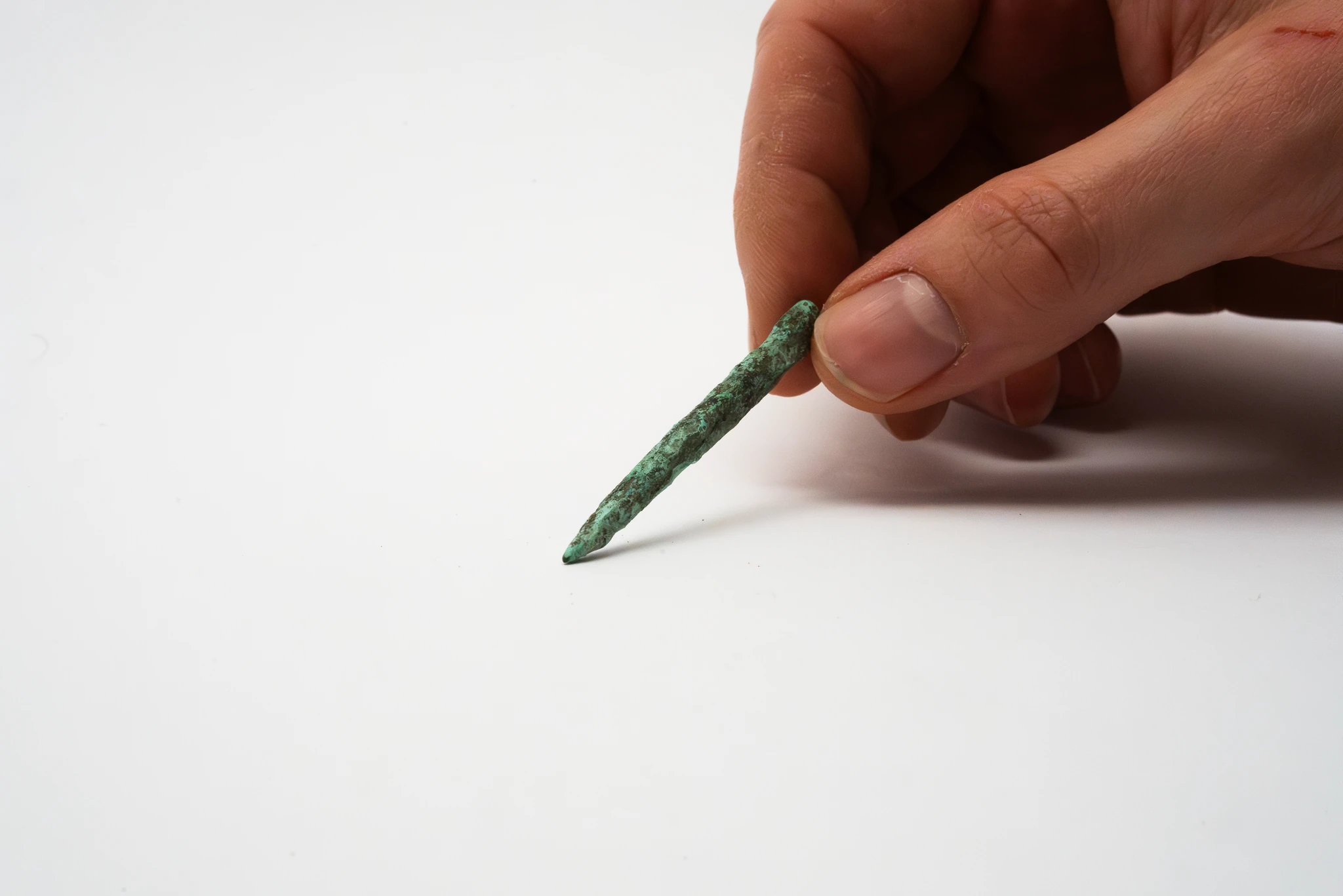 Una mano tiene tra pollice e indice un piccolo oggetto allungato di colore verde, dalla superficie irregolare, appoggiato su uno sfondo bianco