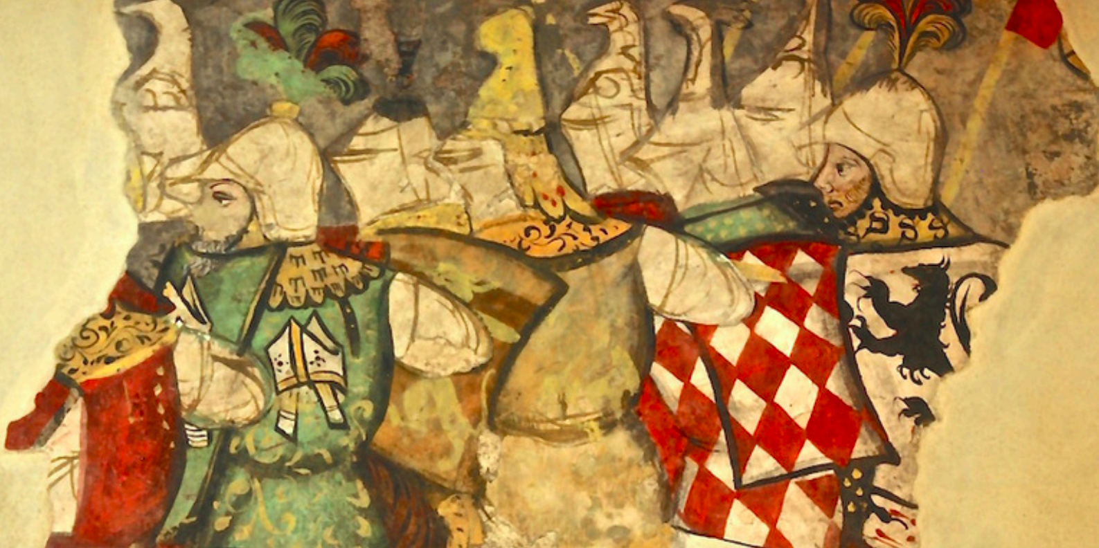 Un affresco medievale danneggiato che raffigura un gruppo di cavalieri armati a cavallo o in processione. I cavalieri indossano elmi bianchi e vesti ornate; uno ha una sopravveste a losanghe rosse e bianche con uno stemma araldico nero. La parete è di intonaco chiaro con bordi irregolari.