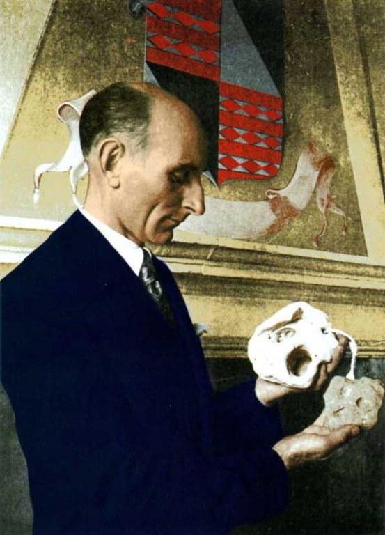 Un ritratto fotografico storico ricolorato del Conte Giuseppe di Ragogna, raffigurato di profilo mentre indossa un abito scuro formale e una cravatta. Il Conte tiene tra le mani ed osserva con attenzione un teschio umano e un frammento di pietra. Sullo sfondo, una parete ospita un grande stemma araldico decorato con motivi a rombi rossi e grigi, affiancato da figure stilizzate. L'immagine ha un'atmosfera solenne e documentaristica, tipica degli studi archeologici del passato.