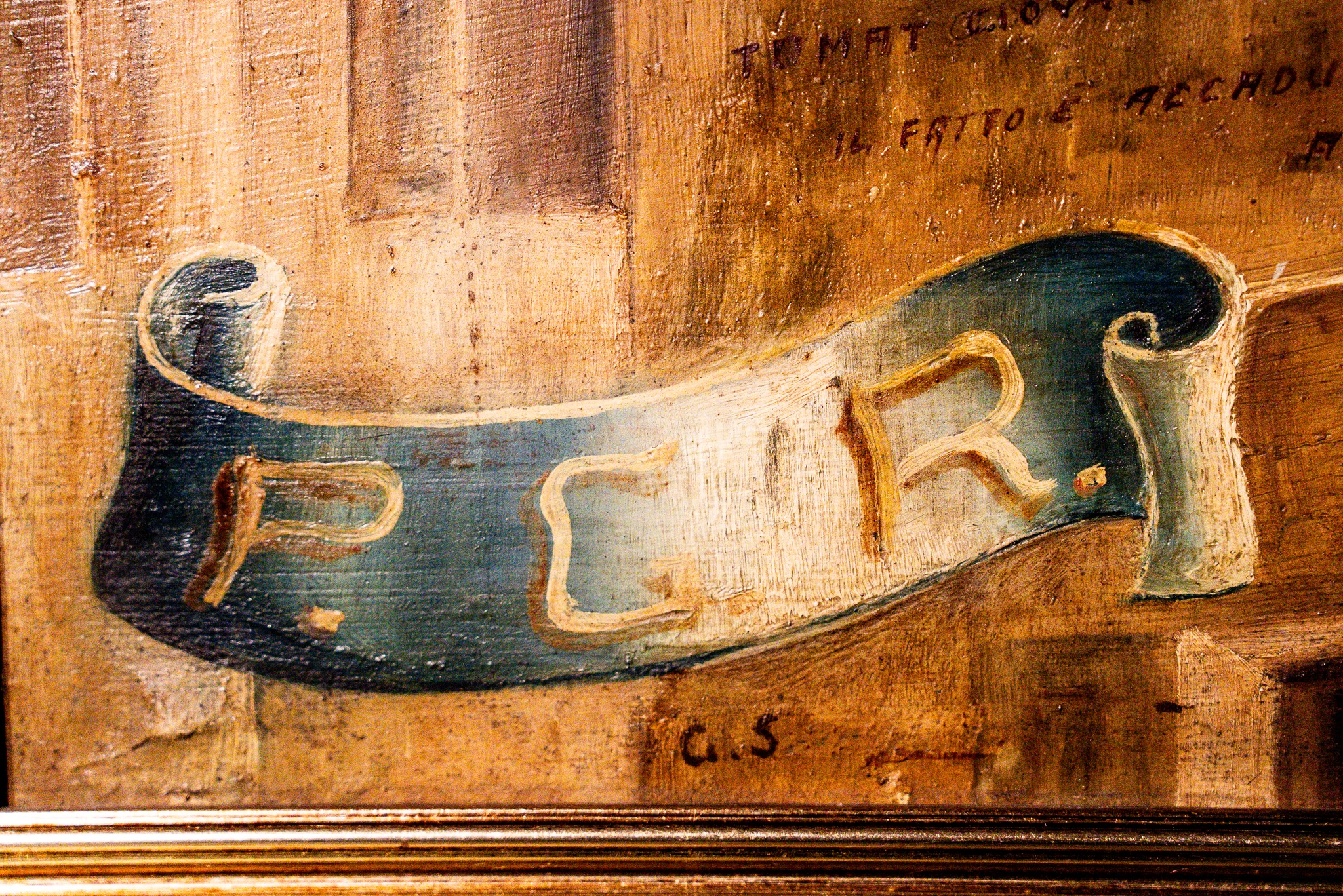 Un dettaglio ravvicinato di un cartiglio dipinto su un ex-voto antico. Il cartiglio, di colore blu sfumato verso il bianco, ha una forma arricciata e reca la sigla "P.G.R." (Per Grazia Ricevuta) scritta in grandi lettere dorate con ombreggiatura scura. Lo sfondo del dipinto è color terra di Siena con pennellate visibili. In alto a destra, sopra il cartiglio, si leggono alcune righe di testo manoscritto in corsivo, parzialmente abrase, che includono le parole "IL FATTO È ACCADUTO". In basso, sotto il cartiglio, appaiono le iniziali "G. S.". La cornice dorata è visibile lungo il bordo inferiore.